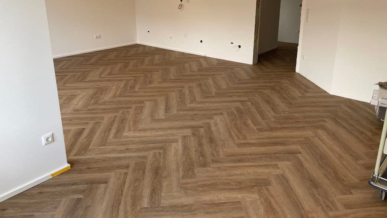 Wohnraum mit fertig verlegtem Fischgrätboden in Eichenoptik, sauber angeschlossen an Wand und Türöffnung